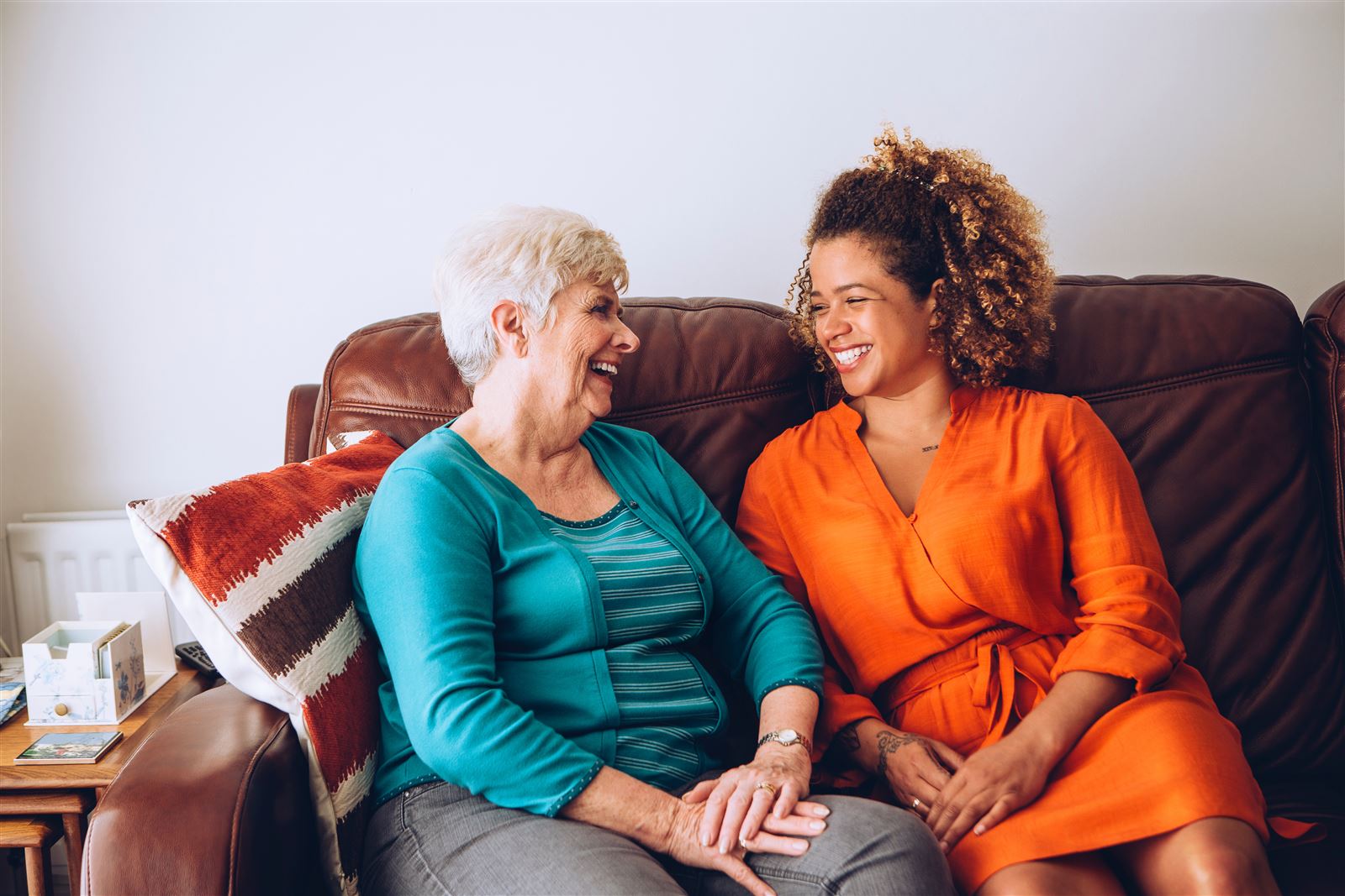 A caregiver and an elderly client laughing together on the sofa